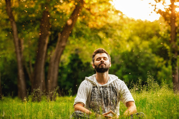 A man sitting on grass in the park and smiling with eyes closed