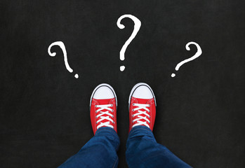 Feet wearing red shoes on black background with question marks.