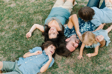 Happy young hipster family having fun while running, bowl,  rising up, piggyback ride their children in park on summer sunset
