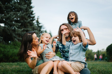 Happy young hipster family having fun, bowl,  rising up, piggyback ride their children in park on summer sunset
