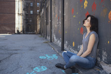 USA, New York City, Young Woman Sitting On The Ground Leaning Against A Wall