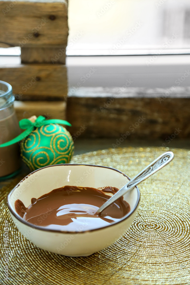 Melted chocolate in glass bowl, on wooden background
