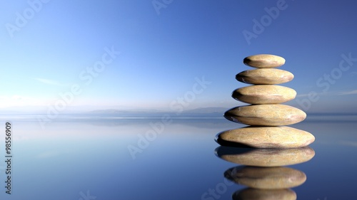 Zen stones stack from large to small in water with blue sky and peaceful landscape background Wallpaper Mural