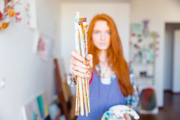 Canvas Print - Paintbrushes holded by young redhead woman painter in artist workshop