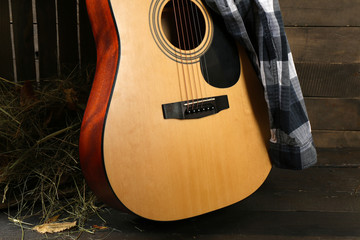 Wall Mural - Acoustic guitar and blue checkered shirt against box with hay on wooden background, close up