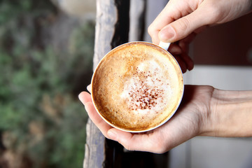 Cup of tasty cappuccino with hands on street background