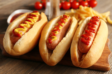 Wall Mural - Tasty hot-dogs with French chips, spices and vegetables on wooden background, close up