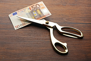 Poster - Golden scissors cut money on wooden background