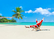 Christmas Santa Claus on deckchair enjoing palm sady ocean beach
