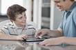© Mint Images - A man and a boy seated looking at a digital tablet and using the touch screen.