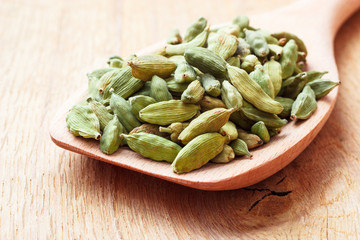 Green cardamom pods on wooden spoon