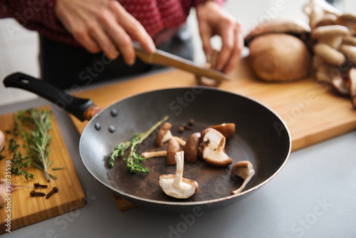 Cuadros en Lienzo Closeup of mushrooms in a frying pan with woman slicing