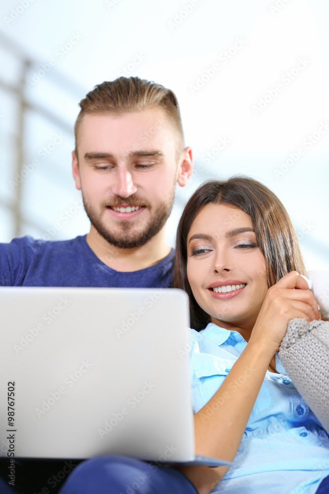 Happy couple sitting on sofa with coffee and working on a laptop