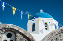 A Blue-domed Greek Orthodox Church With Flags In Oia Town On The Island Of Santorini, Greece