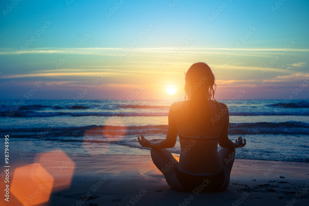 Silhouette young woman practicing yoga on the beach at sunset. - obrazy, fototapety, plakaty 