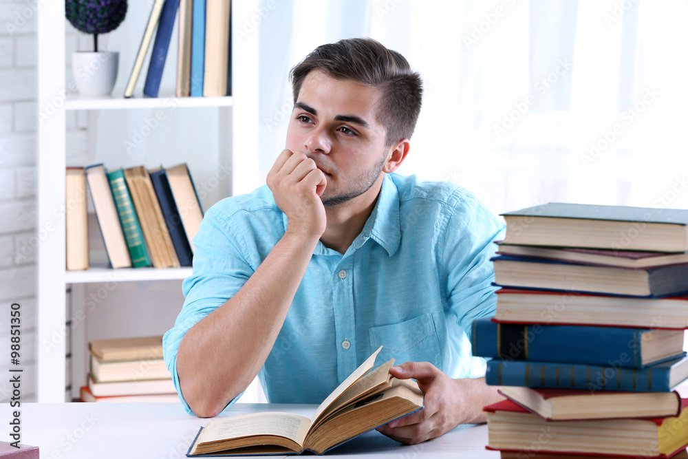 Young man reading book at table in room