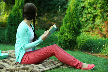 Wall Mural - Young woman with book sitting on green grass outdoors