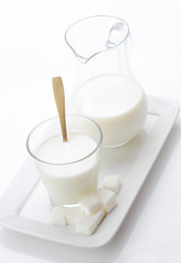 glass of milk with golden spoon and sugar cubes on white backgro