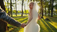 Smiling Bride Holds Groom By The Hand And Runs In A Park