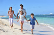 © goodluz - Family of four running on a sandy caribbean beach