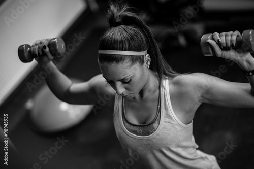 Nowoczesny obraz na płótnie Woman lifting weights and working on her shoulders at the gym