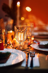 Decorated Christmas holiday table ready for dinner. Beautifully decorated table set with candles, spruce twigs, plates and serviettes for event in the restaurant.