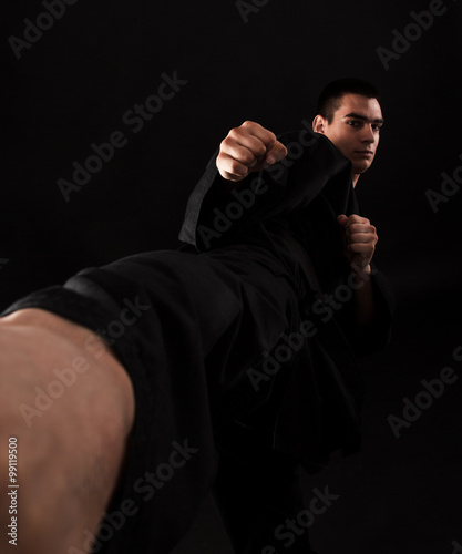 Studio portrait of young karate fighter kicking over black background Фотошпалери