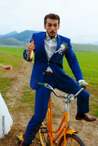 Fotografija drunken groom on a bike holding a beer bottle.