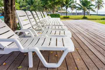 White plastic sunbeds on wooden deck in garden. The outdoor recreation in luxury hotel.