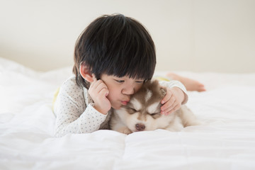 asian child kissing a siberian husky puppy on bed