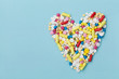 Colorful drug pills in shape of heart on blue background, pharmaceutical concept