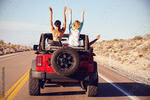 Fotografie, Obraz Rear View Of Friends On Road Trip Driving In Convertible Car
