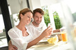 © goodluz - Couple having fun using smartphone at breakfast time