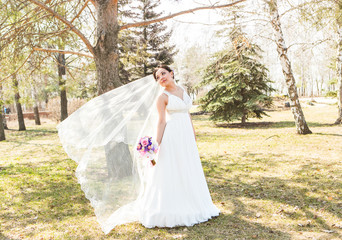   young brunette bride  in the park on nature with a flowing veil.