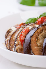 Wall Mural - Baked eggplant with tomatoes, cheese and italian herbs on a white plate, closeup, selective focus .