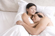 © Blue Jean Images - Asian couple cuddling on bed