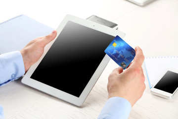 Wall Mural - Man holding credit card and tablet on workplace background