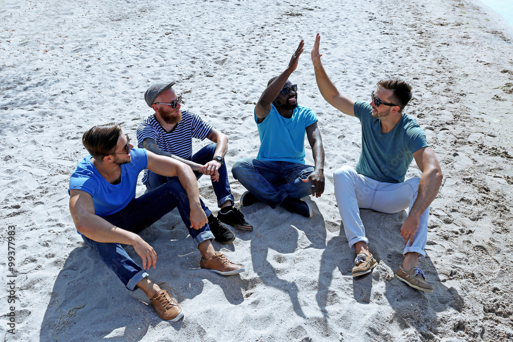 Young men sitting on sand on the riverside
