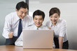 © Blue Jean Images - Young businessmen and businesswoman using laptop in office
