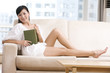© Blue Jean Images - Asian woman reading on a sofa