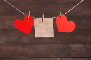 Wall Mural - Paper hearts and empty sheet hanging on cord against wooden background