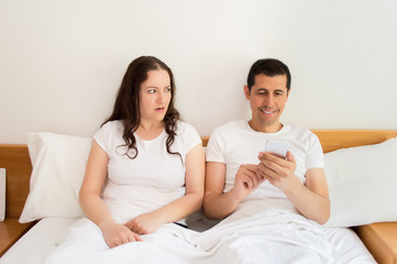 upset with the husband in the bed by the smartphone