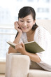 © Blue Jean Images - Asian woman reading on a sofa