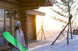 Young woman holding a snowboard in front of a log cabin