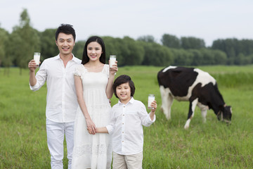 Happy family holding glasses of milk with cattle grazing in the pasture