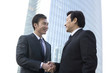© Blue Jean Images - Businessmen shaking hands in front of tall building