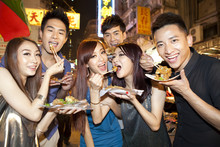 Cheerful Young People Trying Some Local Snacks On Temple Street Of Hong Kong, Night View