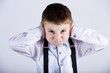 Angry, unhappy, irritated little boy covering ears, looking to camera over white background.