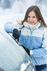 Wall Mural - Beautiful young woman removing snow from her car.