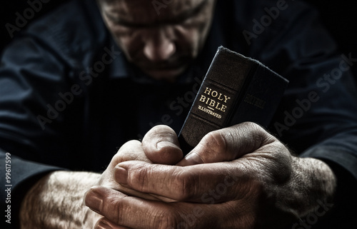 Cuadros en Lienzo Un hombre que ruega sosteniendo una Biblia.